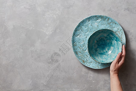 彩色的波塞恩老式手工菜肴灰色大理石桌子上,文字的女人手里着个蓝色的陶瓷碗俯视图传统的纪念品陶瓷手工制作的彩图片
