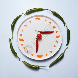 白色盘子,内衬切片辣椒樱桃西红柿,以时钟的形式烹饪的吃食物的时间切片甜椒以时钟的形式放盘子上,背景灰色的图片