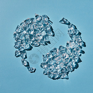 阴阳符号的形状由蓝色背景上阴影的透明人造冰块成的顶部视图蓝色背景上以阴阳符号的形式的碎冰块的风景图片