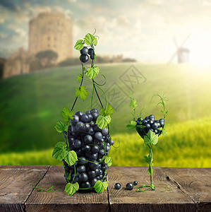 瓶葡萄酒杯由葡萄叶串葡萄制成的木制背景,背景模糊的城堡,磨坊绿色的草坪瓶葡萄酒杯由葡萄叶串葡萄制成的木图片