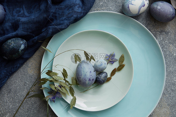 复活节鸡蛋与绿色植物装饰盘子上用蓝布烤复活节彩蛋图片