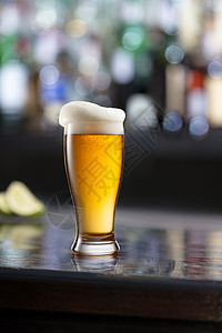 杯啤酒,泡沫黑色的木制桌子上,酒吧的模糊酒吧背景上木制桌子上的杯啤酒模糊的背景图片