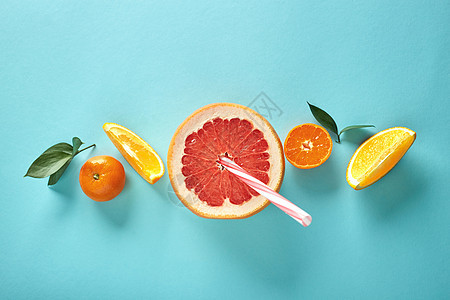 橘子柑橘葡萄柚中新鲜榨出的果汁冰沙的原料排列蓝色背景上,平躺着橙色片半的葡萄柚,蓝色背景上用吸管图案图片