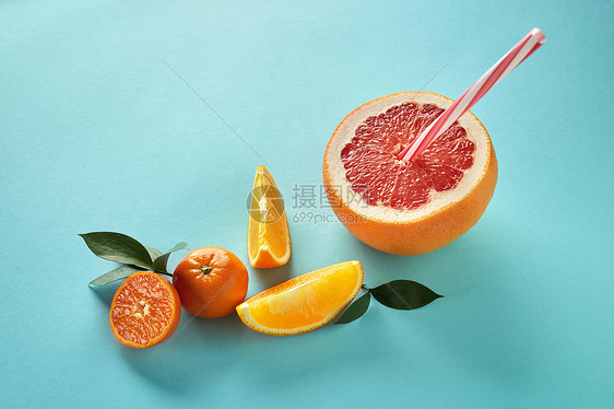 热带外来柑橘类水果半个葡萄柚,橘子,橘子片与塑料吸管果汁蓝色的纸背景异国情调的柑橘类水果,绿叶塑料吸管果汁蓝色的纸背景图片