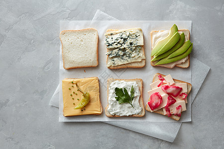 各种素食土司三明治与奶酪,鳄梨,卷心菜胡椒羊皮纸上的灰色混凝土背景健康早餐图片