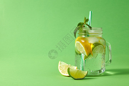 夏天清爽的饮料绿色的背景上自制的泡鸡尾酒加冰,石灰柠檬片,绿色的薄荷叶与塑料吸管璃罐梅森罐与新鲜的自制泡柠檬水图片