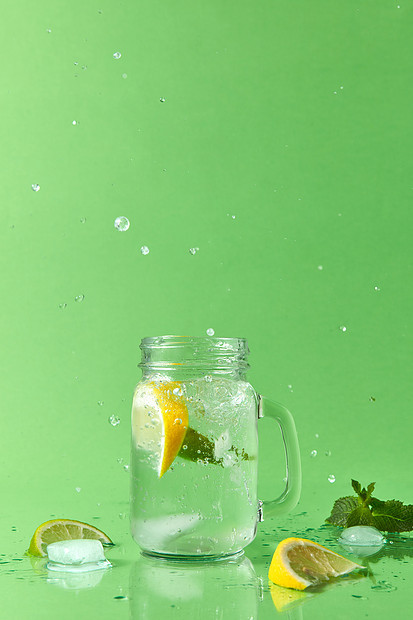 绿色桌子上的璃罐,自制的泡柠檬水柠檬片,绿色的薄荷叶把柠檬水璃杯里溅出来图片