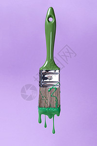 用绿色油漆刷,刷子上滴下的油漆滴紫色的背景上刷绿色油漆,图片