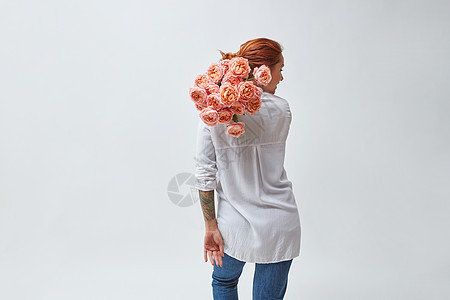 个穿着牛仔裤手臂上纹身的女人,肩上着粉红色的媒体玫瑰,母亲节,情人节鲜花的女人母亲节图片