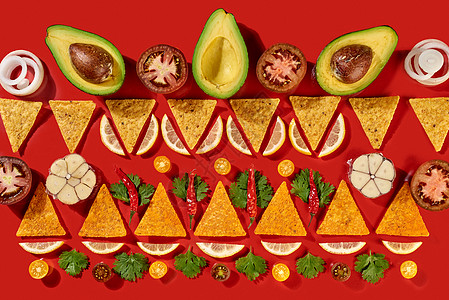 墨西哥玉米片鳄梨半片,柠檬片,大蒜,柠檬片大蒜番茄部分洋葱欧芹绿色红色背景上的传统图案顶部视图创意几何食品图片