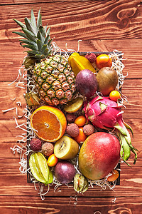 夏季异国水果个盒子与新鲜多汁的成分杨桃,菠萝,龙果,芒果,荔枝,菲萨利斯,橙色,猕猴桃,金橘,西番莲木制背景顶部景观图片
