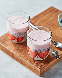两杯冰沙桑椹片,CHIA种子个木板上的灰色背景健康饮食的分层酸奶,自制甜点与成熟草莓,辣椒布丁璃木制背景图片