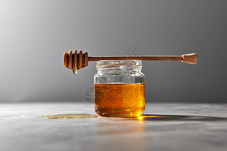 将机天然新鲜蜂蜜璃壶滴灰色的石头背景上,放置文本下传统用的甜度芳香的天然机蜂蜜木棒滴灰色的厨房桌子上图片