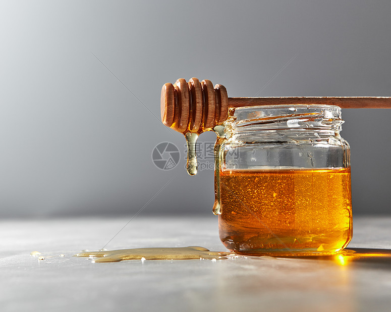 机甜花Hohey蜂蜜滴入璃壶的灰色背景,放置文字纯天然甜味璃壶中滴下机天然新鲜蜂蜜灰色的厨房桌子上罗什哈图片