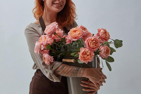 带纹身的棕色围裙上的微笑女孩灰色背景上的花瓶里着美丽的粉红色玫瑰花,文字的情人节的轻的红发女孩,图片