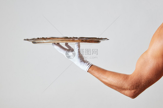 肌肉发达的侍者手戴着只白色手套,手里着个银色的老式空托盘,背景白色的,文字的地方侍者用肌肉发达的手戴着只白色手套,图片