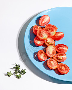 多汁的机樱桃西红柿茎上剥离,灰色背景上的蓝色盘子中,阴影的反射的风景将成熟的西红柿减半,放灰色背景图片