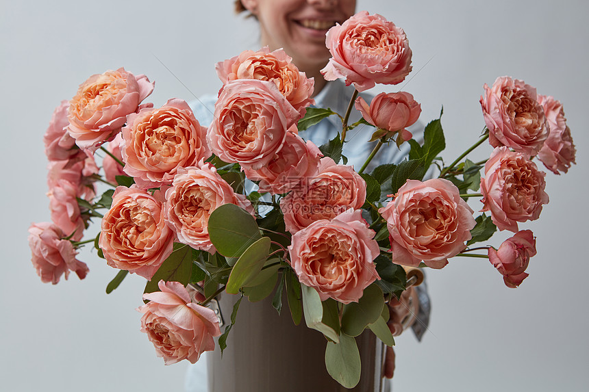 快乐的微笑女孩,灰色背景上粉红色的玫瑰送给母亲节的礼物美丽的粉红色玫瑰,把个女人抱灰色的背景上母亲节图片