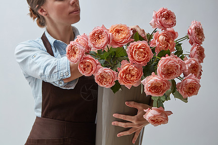 粉红色玫瑰的花瓶个微笑的女人着花店,着灰色背景上的粉红色玫瑰商业花卉的女孩花店,大粉红色玫瑰围绕灰图片