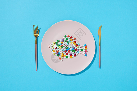 许多同的药丸补充剂食物圆形白色盘子与叉子刀减肥药补充剂的饮食顶部视图彩色胶囊药丸,以鱼的形式盘子图片