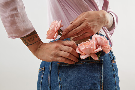 轻的女孩穿牛仔裤,裤子粉红色衬衫,后放个口袋里的天然花,玫瑰灰色的背景,地方为文字的女人母亲的天精致图片