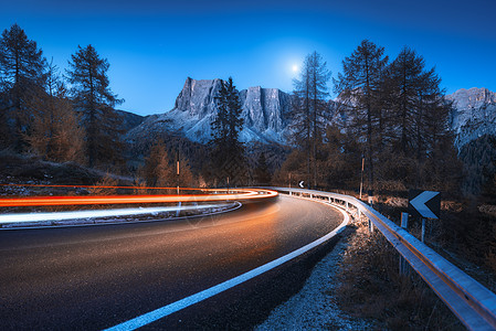 秋天的夜晚,蜿蜒的道路上模糊的汽车前灯风景与沥青道路,轻小径,山脉,树木,蓝天与月亮黄昏意大利的巷道看公路岩石图片