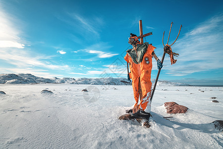 稻草人穿着橙色的衣服,戴着三叉戟的防具,着蓝天,云彩雪域冬季景观与趣的假人,石头雪山脉泰伯卡,俄罗斯旅行图片