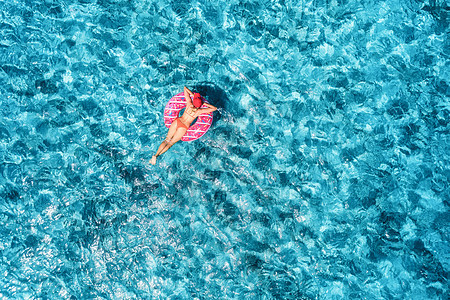 阳光明媚的日子里,苗条的轻女子蓝色的大海里游泳,粉红色的甜甜圈上游泳热带航空景观与女孩,清澈的水欧洲的风景图片
