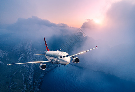客机日落时飞过云层风景与白色飞机,低云,海岸,紫色的天空黄昏飞机正降落出差商业飞机旅行空中视野图片
