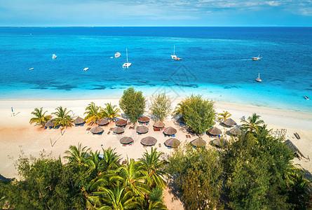 阳光明媚的日子里,印度洋的沙滩上俯瞰雨伞棕榈树非洲桑给巴尔的暑假热带景观,棕榈树,阳伞,船,游艇,蓝色的水图片