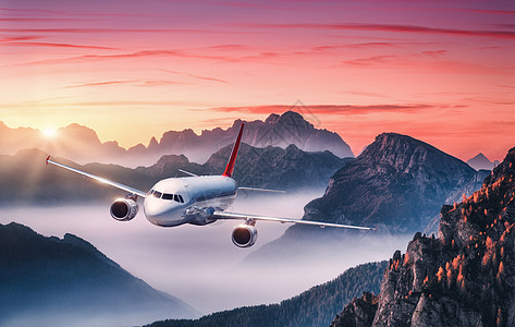 飞机夏天五彩缤纷的日落时,雾中飞过群山风景与客机,山丘低云,红色的天空白色飞机商务旅行商业飞机空中视野图片