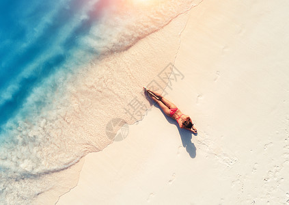 蔚蓝的大海附近的沙滩上,美丽的轻躺着的女人日落时带着波浪的鸟瞰暑假顶部的背运动苗条的女孩,清澈的水感的图片