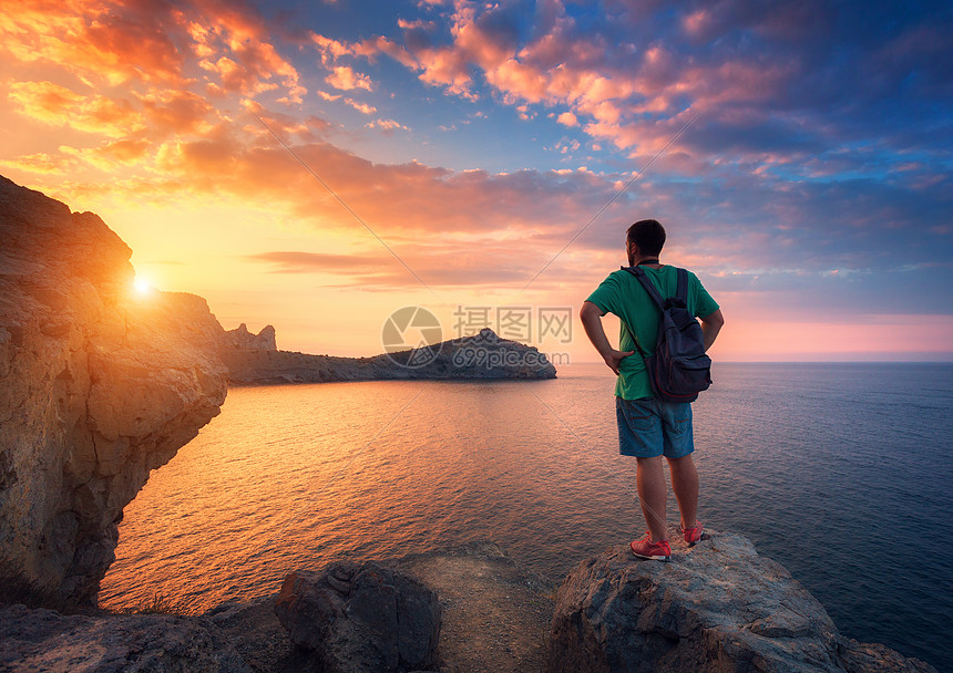 美丽的夏季景观与站立的人与背包石头海洋与彩色天空与云彩日落旅行背景运动,生活方式旅游业图片