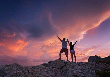 风景与个站立的轻人女人的轮廓山峰上五颜六色的日落美丽多云天空背景上的男人女孩人们的剪影夫妇旅行图片