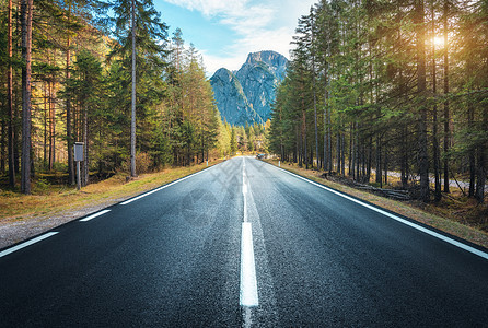 意大利日落时的夏季森林道路美丽的山路,绿树阳光景观与空沥青路林地,蓝天,高岩石欧洲旅行图片