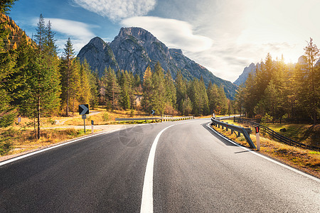 意大利日落时的夏季森林道路美丽的山路,绿树阳光景观与空沥青路林地,蓝天,高岩石欧洲旅行图片