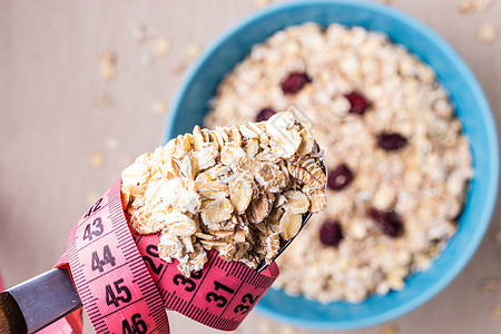 饮食健康食品减肥理念蓝色碗里的燕麦片厨房桌子上勺子周围的粉红色测量带,顶部的风景图片