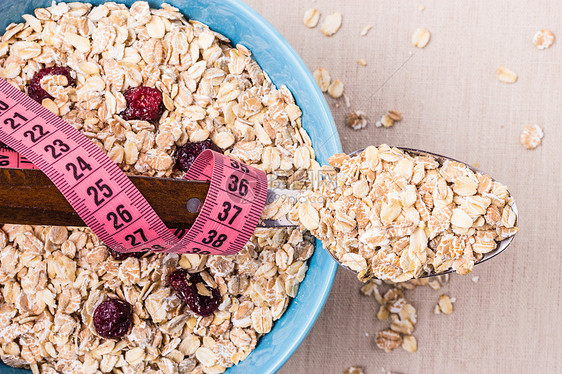 饮食健康食品减肥理念蓝色碗里的燕麦片厨房桌子上勺子周围的粉红色测量带,顶部的风景图片