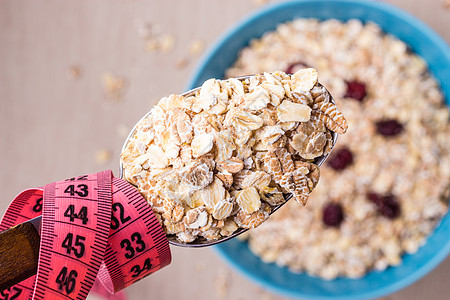 饮食健康食品减肥理念蓝色碗里的燕麦片厨房桌子上勺子周围的粉红色测量带,顶部的风景背景图片