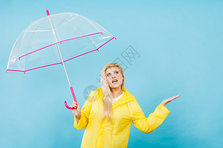 金发女人戴着黄色雨衣,着透明的雨伞检查天气,如果下雨的话图片