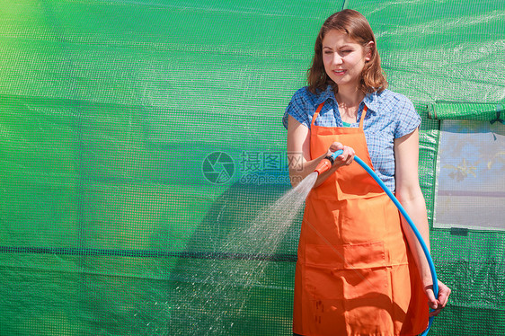 园艺穿着橙色围裙的女人着灌溉植物的喷水软管,室外浇灌花园图片