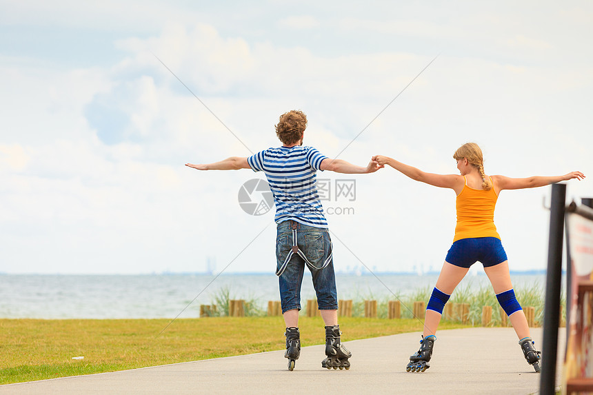 节日,积极的人友谊的轻的穿着溜冰鞋的夫妇骑海边的户外,女人男人长廊上滑行图片