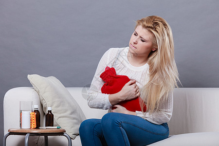 疼痛期月经痉挛问题的女人胃抽筋,坐沙发上,感觉很舒服,着热水瓶,感觉