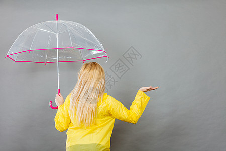 金发女人穿着黄色雨衣,着透明的雨伞,检查天气否下雨背景穿雨衣的女人着雨伞检查天气图片