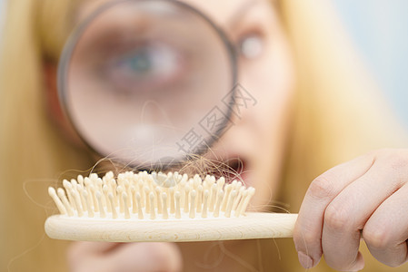 女人用放大镜看着她的刷子检查脱发,理发女人放大头发刷图片