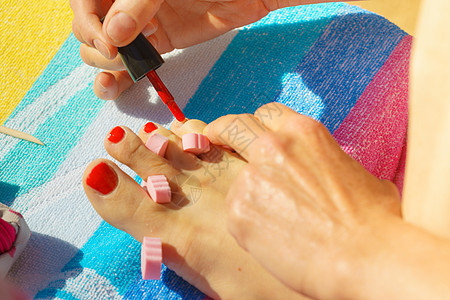 女人放松她的足疗与红色指甲油海滩毛巾女照顾脚女人用红色指甲油修脚图片