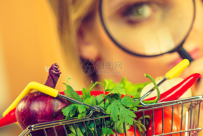 女人用放大镜,用许多五颜六色的蔬菜调查购物篮健康的饮食生活方式,营养素食,寻找虫剂化学品调查蔬菜购物背景的妇女图片