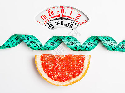 节食健康饮食减肥理念用白色重量秤上的测量带特写葡萄柚切片图片
