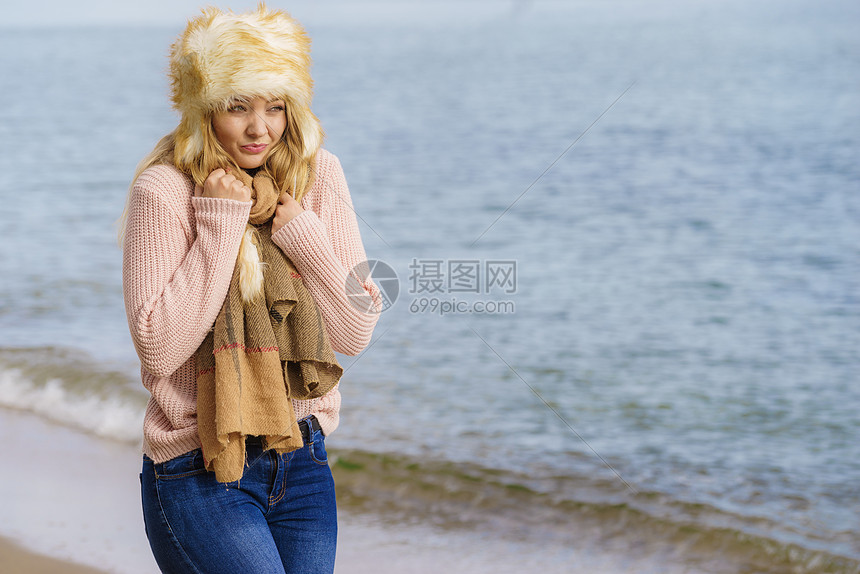 女人穿着温暖时尚的秋装,戴着毛茸茸的大帽子,但感觉很冷女海滩上放松散步时发冷穿着时尚服装的女海边感觉很冷图片