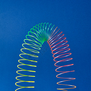 蓝色背景上以抛物线的形状蓝色背景上编彩色玩具螺旋蓝色背景上的柔塑料彩虹弹簧图片